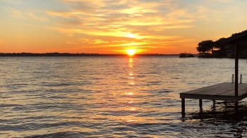 A sunset over a lake with silhouettes of trees and a wooden pier.