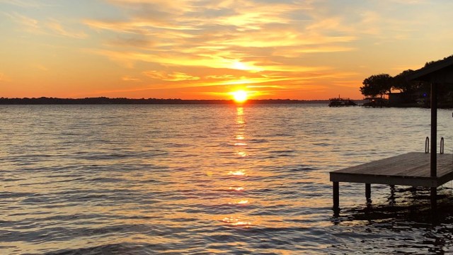A sunset over a lake with silhouettes of trees and a wooden pier.