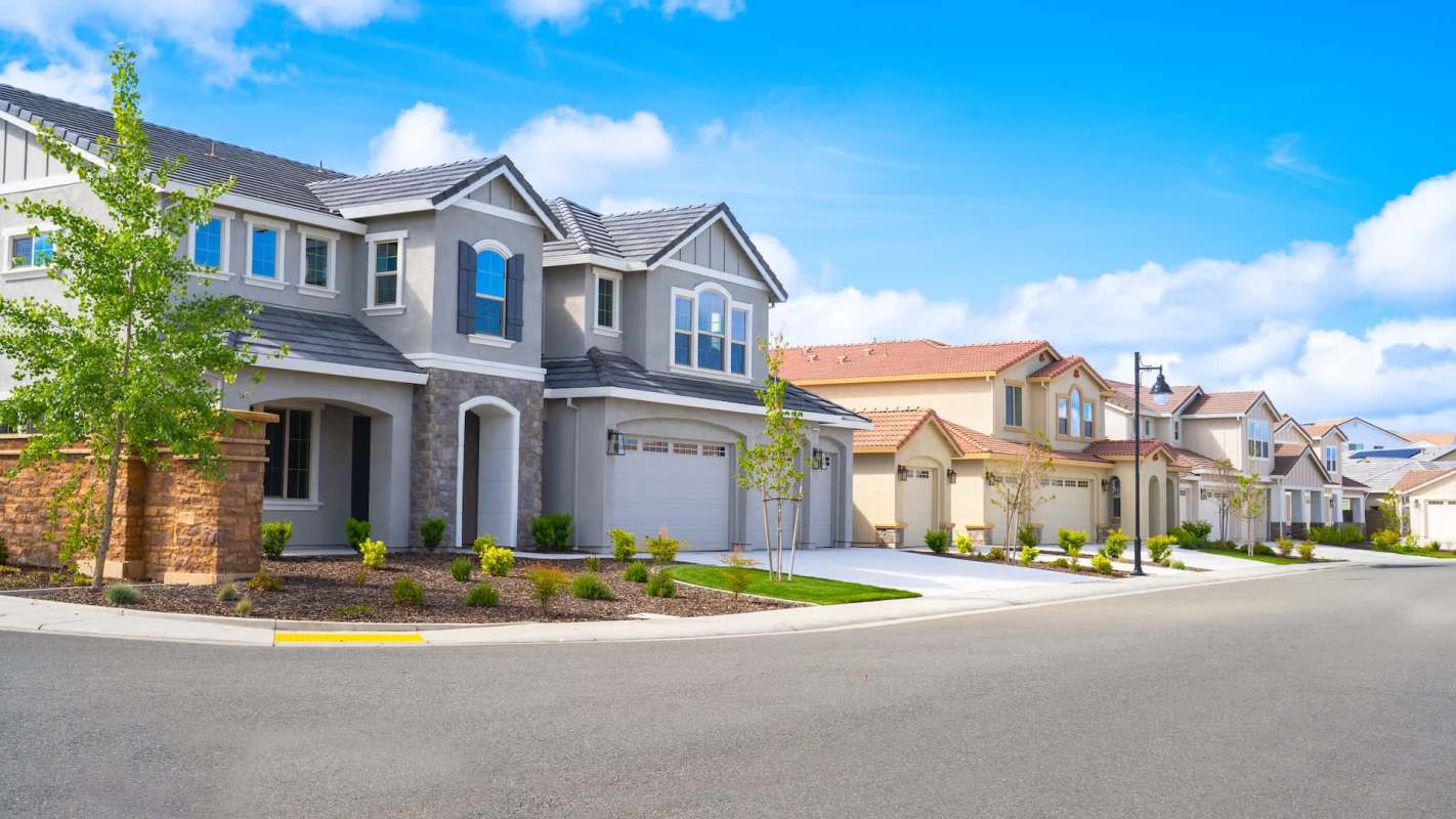 A quiet neighborhood with modern homes lining a curved street under a bright blue sky.