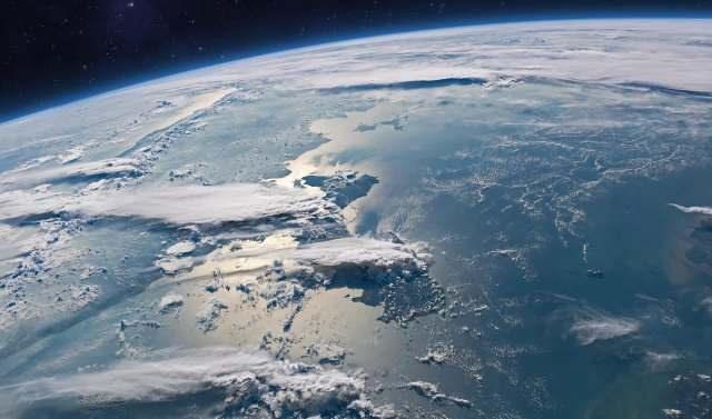 A view of Earth from space, showcasing clouds and reflections on the ocean surface.
