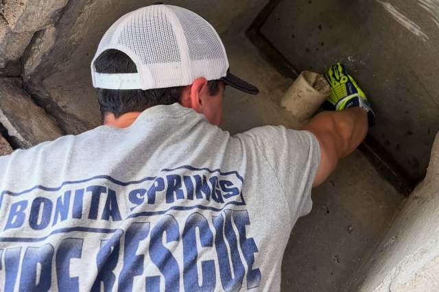 A rescue worker reaching into a storm drain.