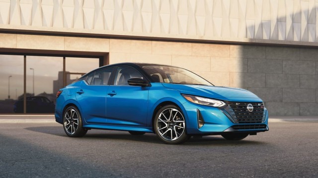 A bright blue sedan parked in front of a modern building with geometric patterns.