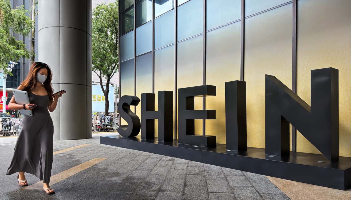 A woman in a long dress walking past a Shein sign.