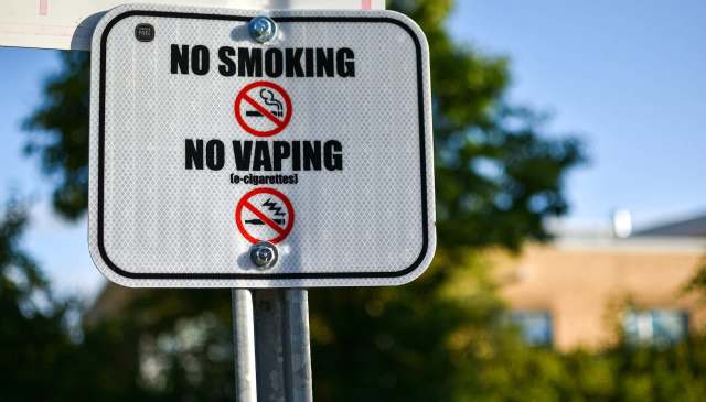 A sign stating "No Smoking" and "No Vaping" with corresponding graphics, placed outdoors.