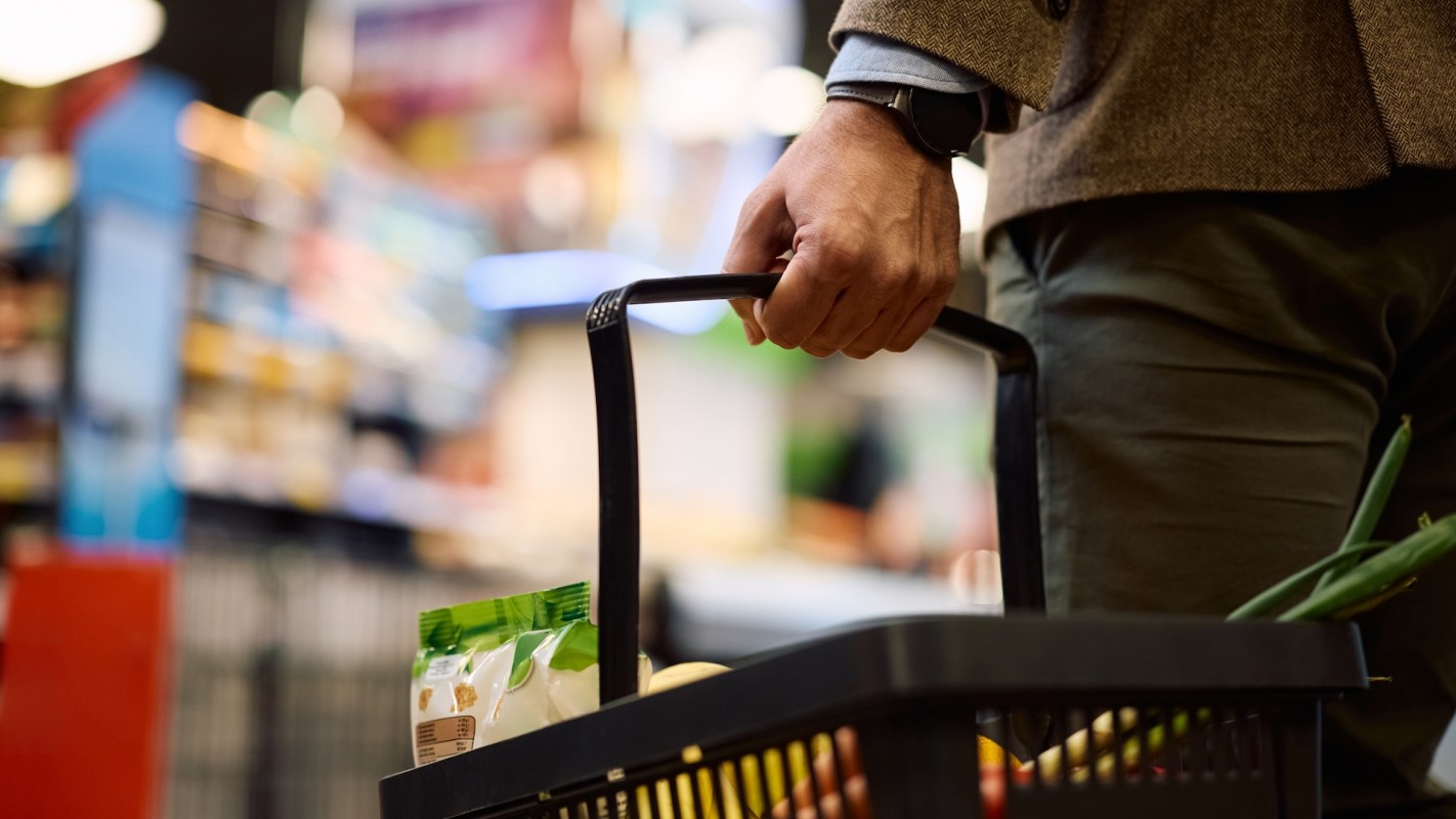 A person holds a shopping basket filled with groceries in a busy store.