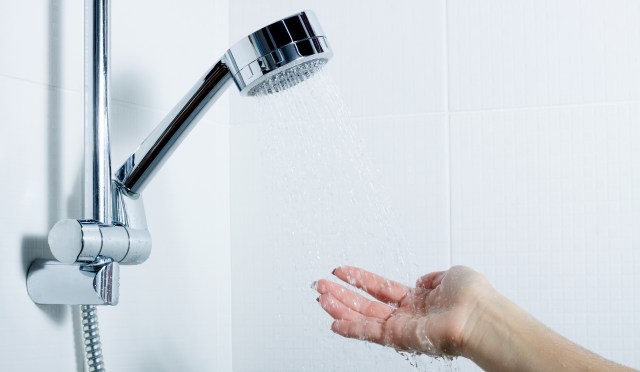A hand is extended under a showerhead, with water cascading down onto the palm.