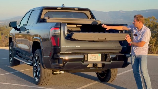 A person demonstrates the features of a GMC Hummer EV truck while standing next to its open tailgate.