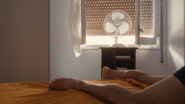 A person's bare feet extend from a bed, with a fan and window in the background.