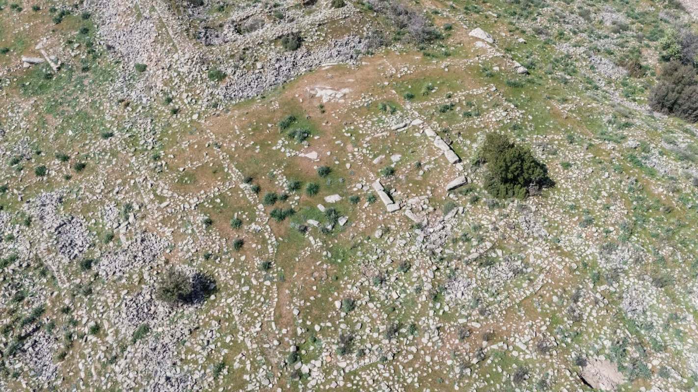 An aerial view of a rocky, grass-covered landscape featuring ancient ruins and sparse vegetation.