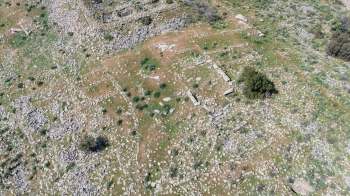 An aerial view of a rocky, grass-covered landscape featuring ancient ruins and sparse vegetation.