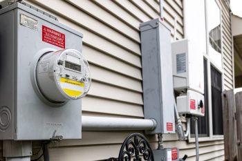 An electric meter and power boxes mounted on the exterior wall of a house.