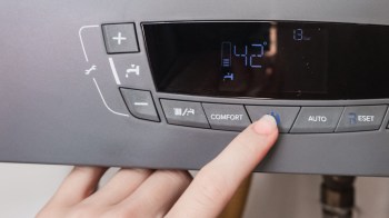 A person's hand adjusts the control panel of a heating device displaying temperature and pressure readings.