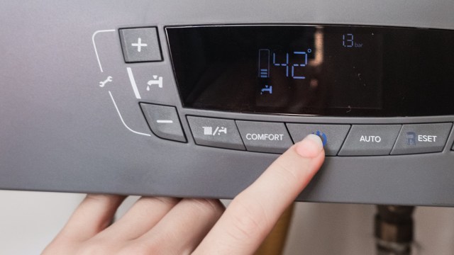 A person's hand adjusts the control panel of a heating device displaying temperature and pressure readings.