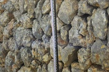 A black and white snake dangling in front of rocks.
