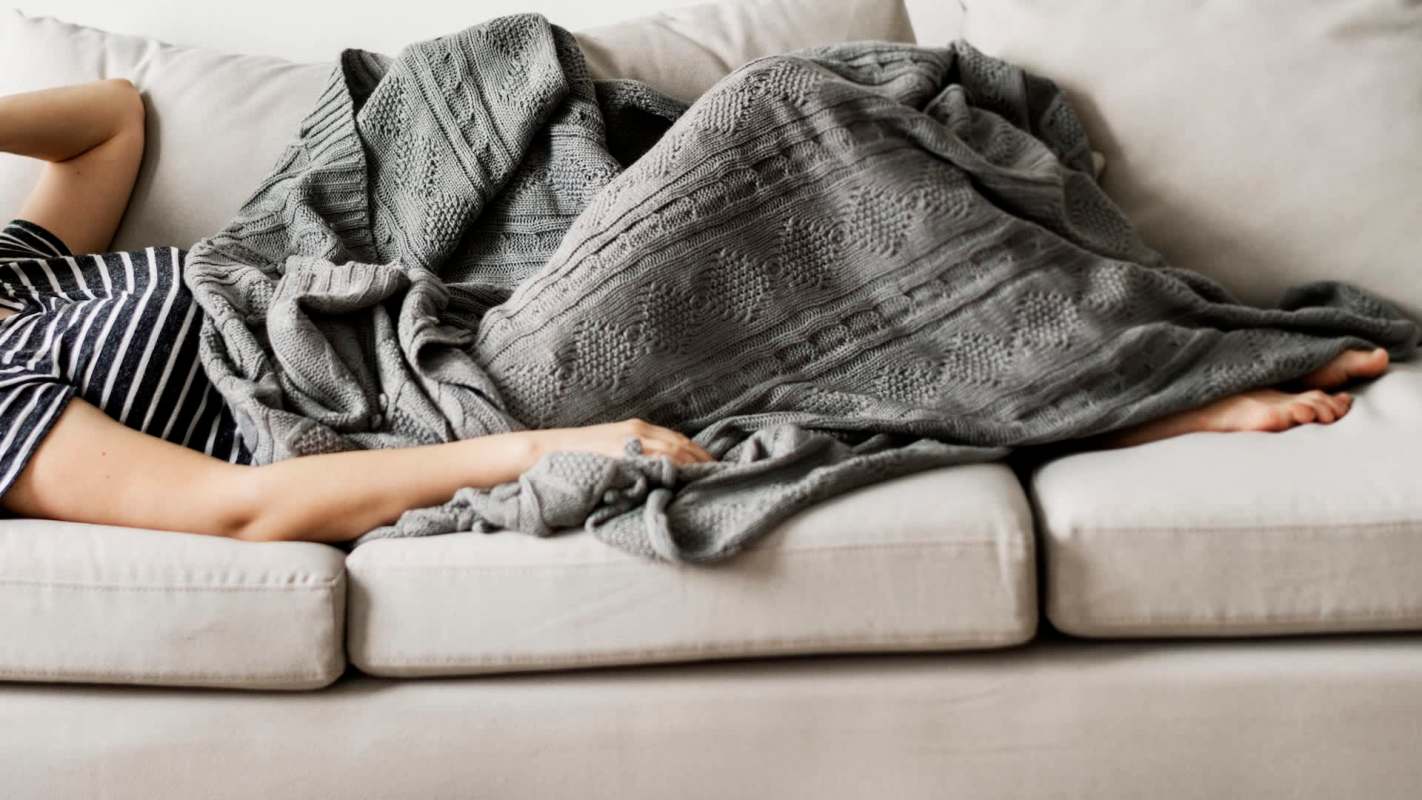 A person with a blanket lying on a couch.