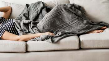 A person with a blanket lying on a couch.