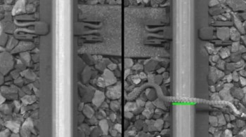 A snake is slithering along railway tracks over gravel.