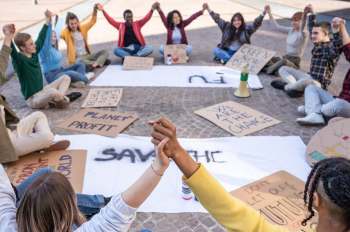 A diverse group of people holding hands in a circle, surrounded by protest signs about climate change.