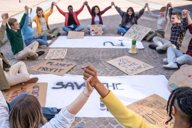 A diverse group of people holding hands in a circle, surrounded by protest signs about climate change.