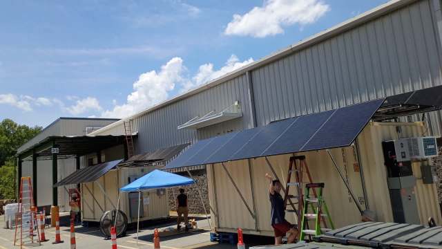 Workers installing solar panels on a building with blue skies and clouds in the background.