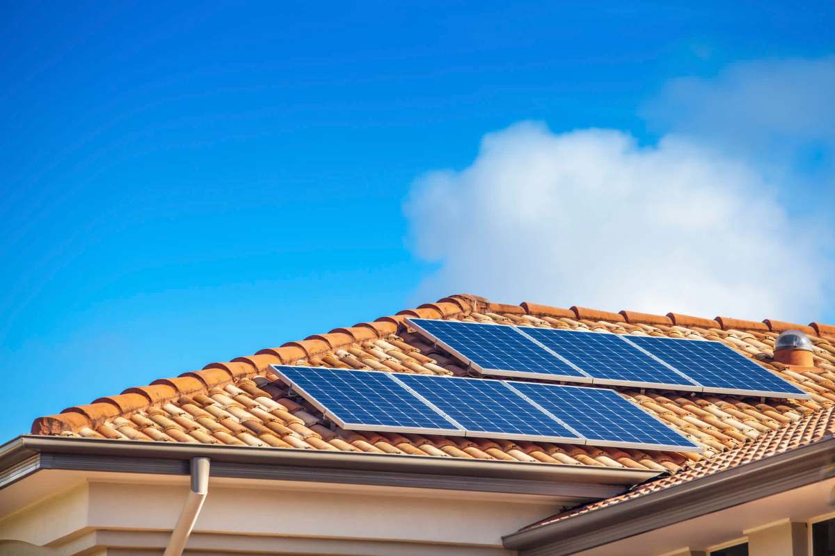 Solar panels installed on a terracotta roof against a clear blue sky.