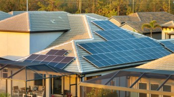 A roof with multiple solar panels installed, overlooking a patio and neighboring houses.