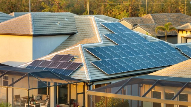 A roof with multiple solar panels installed, overlooking a patio and neighboring houses.