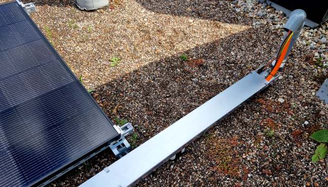 A close-up view of a solar panel connected to a cable conduit on gravel ground.