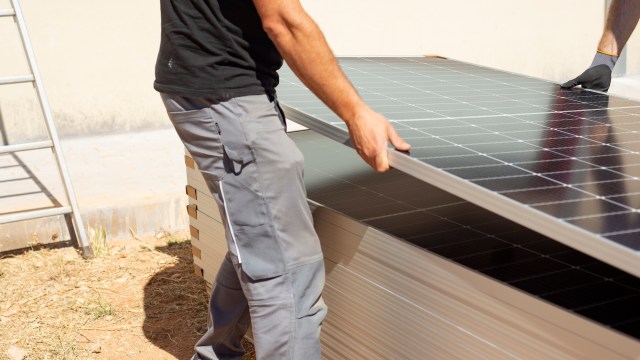 A person is lifting a solar panel from a stack, preparing for installation outdoors.