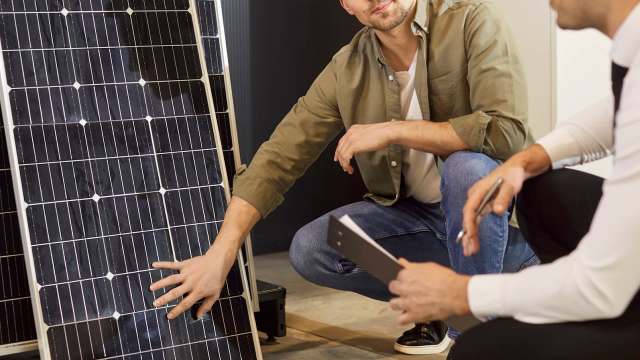 Two men examine a solar panel while discussing its features.