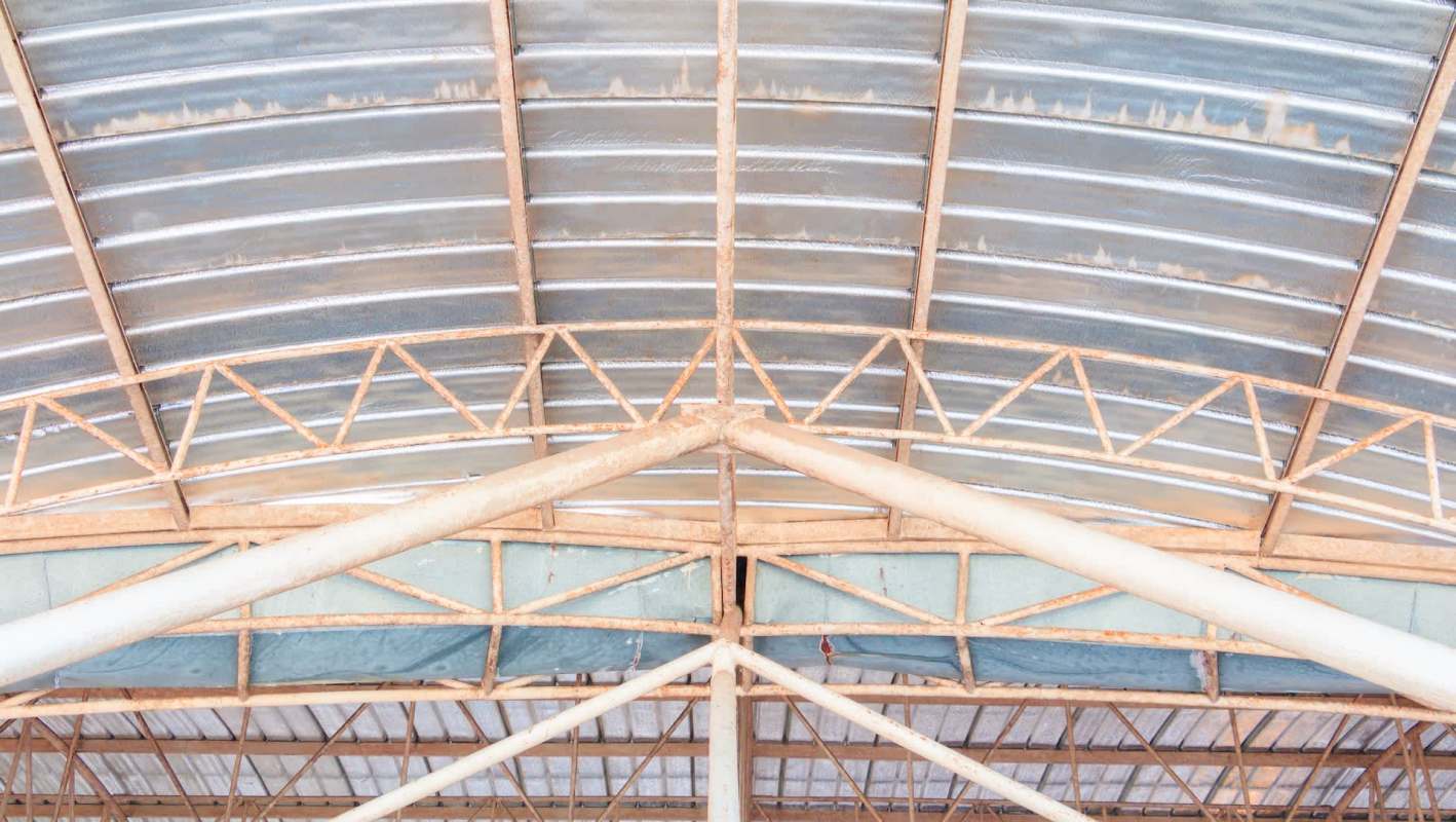 A close-up view of a metal industrial roof structure featuring beams and corrugated panels.