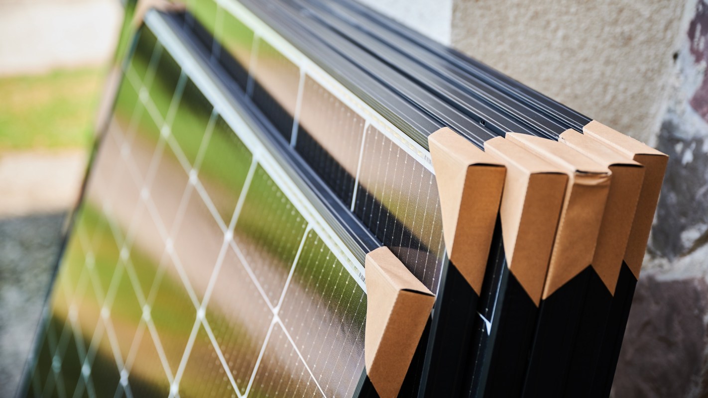 Stacked solar panels with cardboard edge protectors.