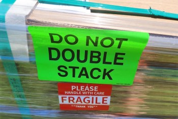 Bright warning labels state "DO NOT DOUBLE STACK" and "PLEASE HANDLE WITH CARE FRAGILE" on a wrapped shipment.