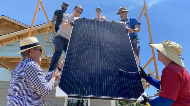 A group of people working together to install a solar panel on a building under a clear blue sky.