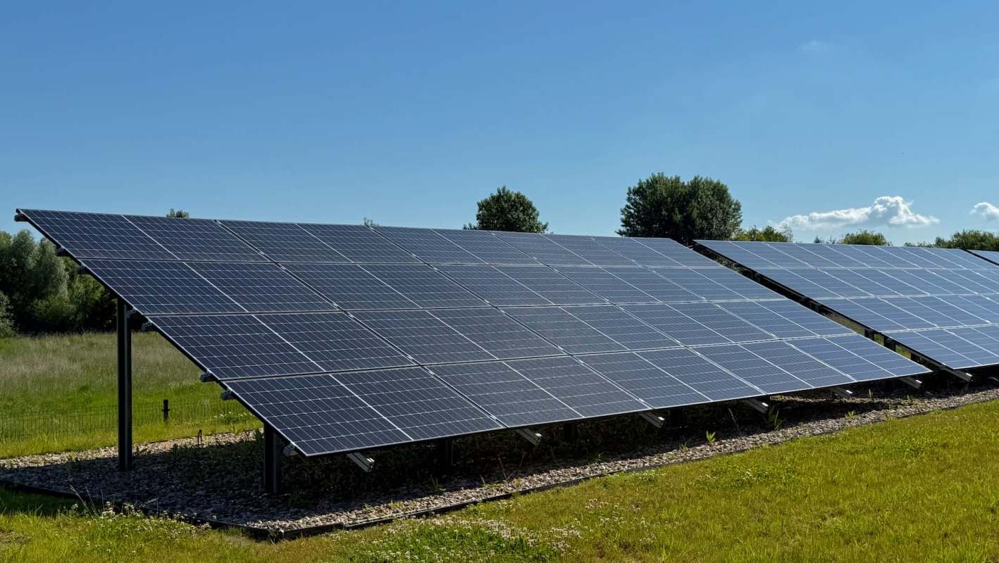 A row of solar panels installed on a grassy field under a clear blue sky.