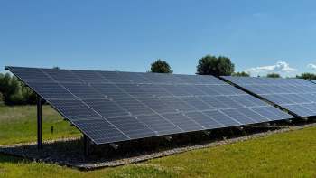 A row of solar panels installed on a grassy field under a clear blue sky.