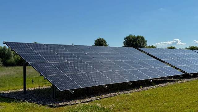 A row of solar panels installed on a grassy field under a clear blue sky.
