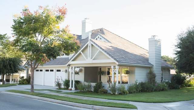 A charming suburban house with a porch, manicured lawn, and large trees on a quiet street.