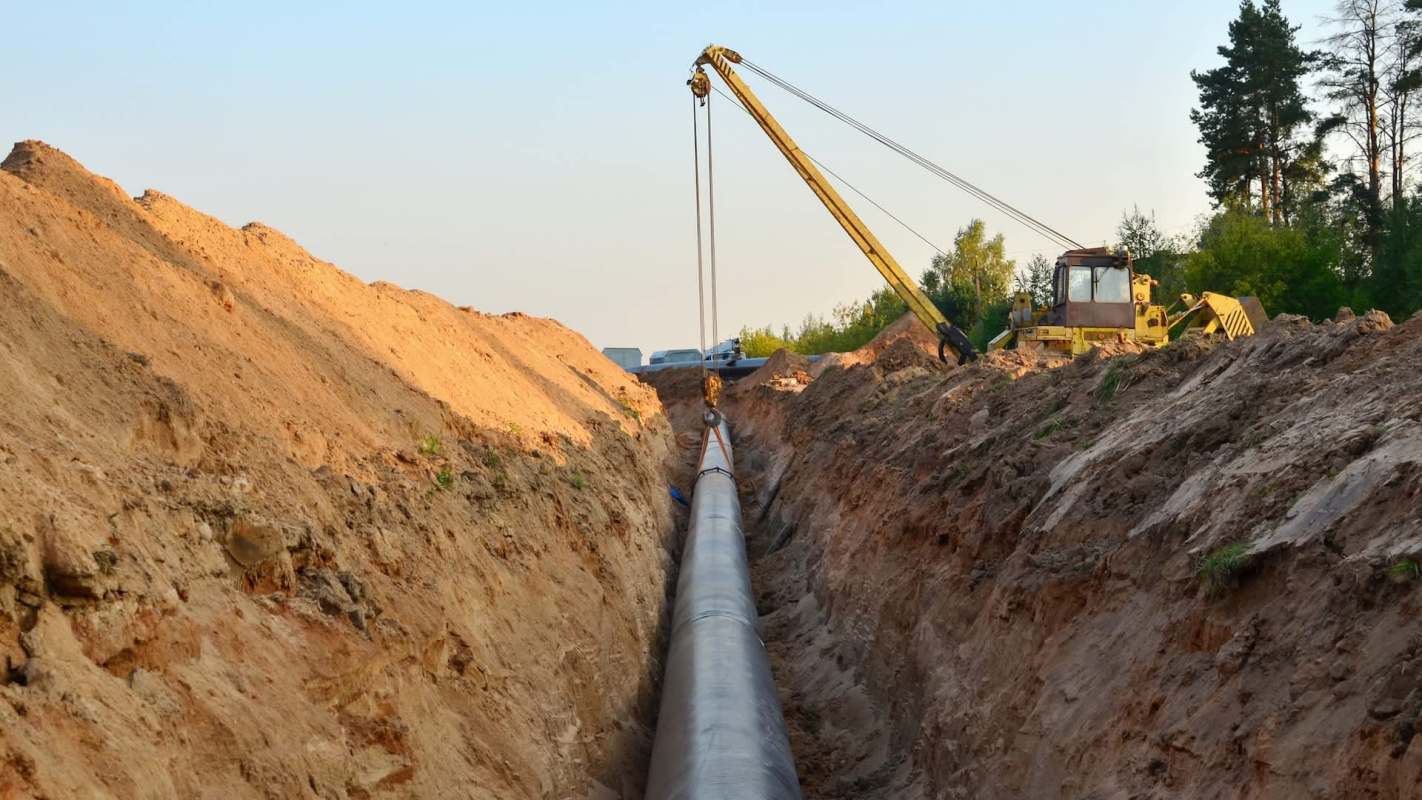 A construction site with a long pipeline being installed in a trench, surrounded by dirt and machinery.