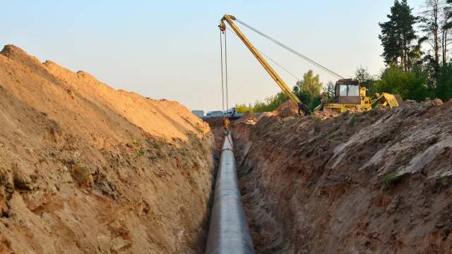 A construction site with a long pipeline being installed in a trench, surrounded by dirt and machinery.