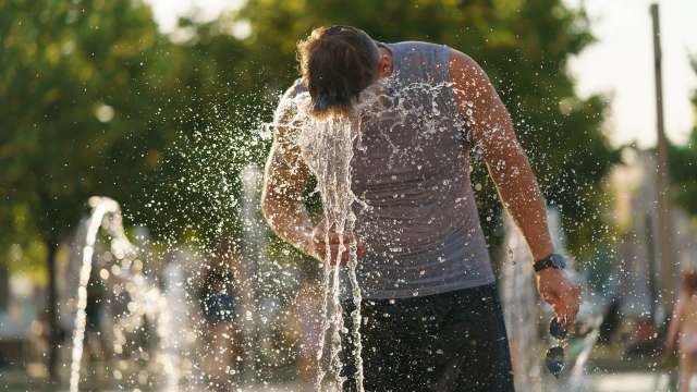 A man splashes water from a fountain onto himself in the summer.