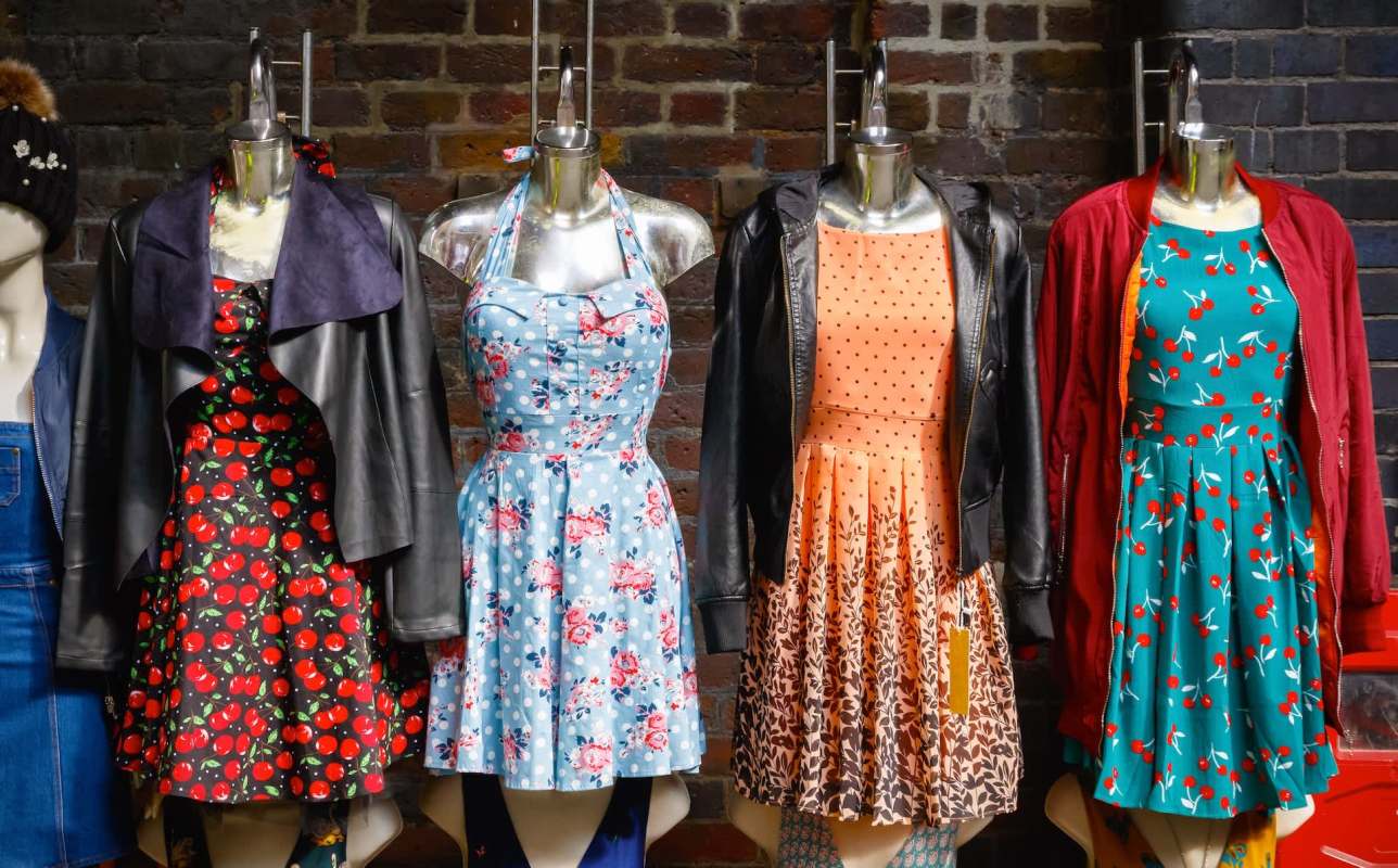 A display of colorful dresses on mannequins against a rustic brick wall.