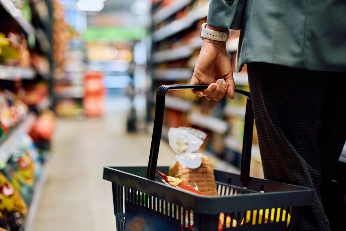 A person carrying a shopping basket in a grocery store.