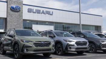 A lineup of Subaru vehicles in front of a modern dealership with the Subaru logo prominently displayed.