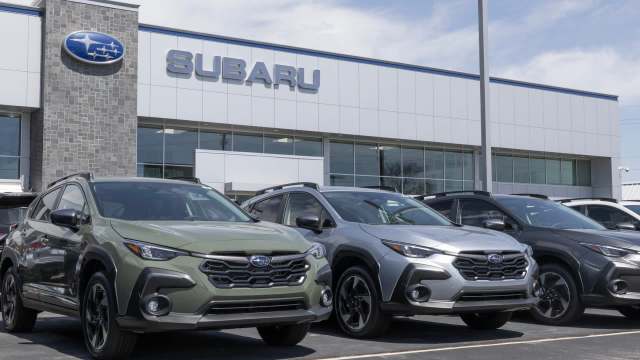 A lineup of Subaru vehicles in front of a modern dealership with the Subaru logo prominently displayed.