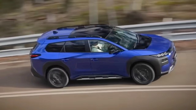 A blue SUV driving on a winding road with a blurred background, suggesting motion.