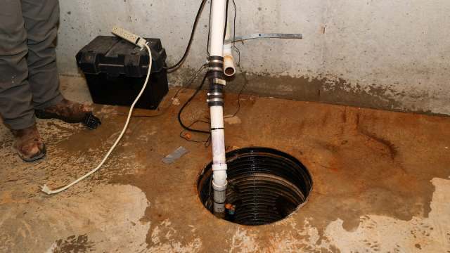 A sump pump system is installed next to a circular drainage pit in a concrete basement.
