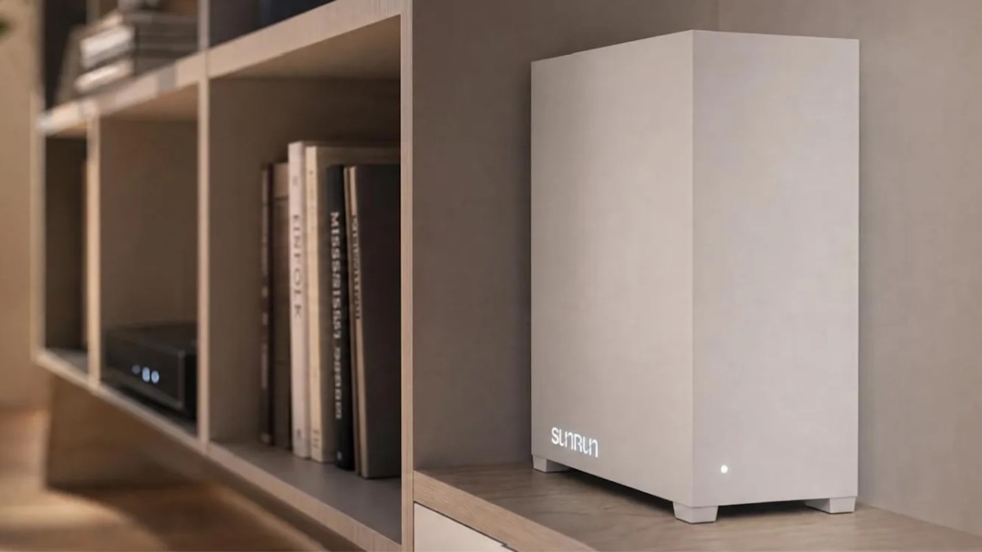A modern, minimalist white device with a Sunrun logo sits on a shelf next to books in a stylish living room setting.