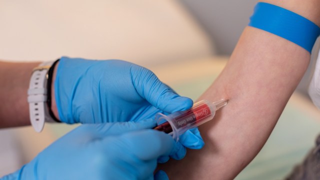 A healthcare professional draws blood from a patient's arm while wearing blue gloves.