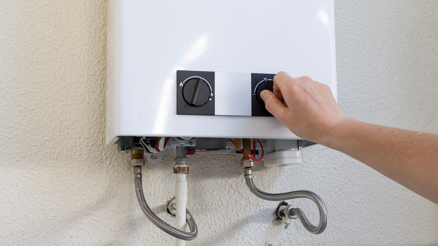 A person adjusting the knobs on a white tankless water heater mounted on a wall.